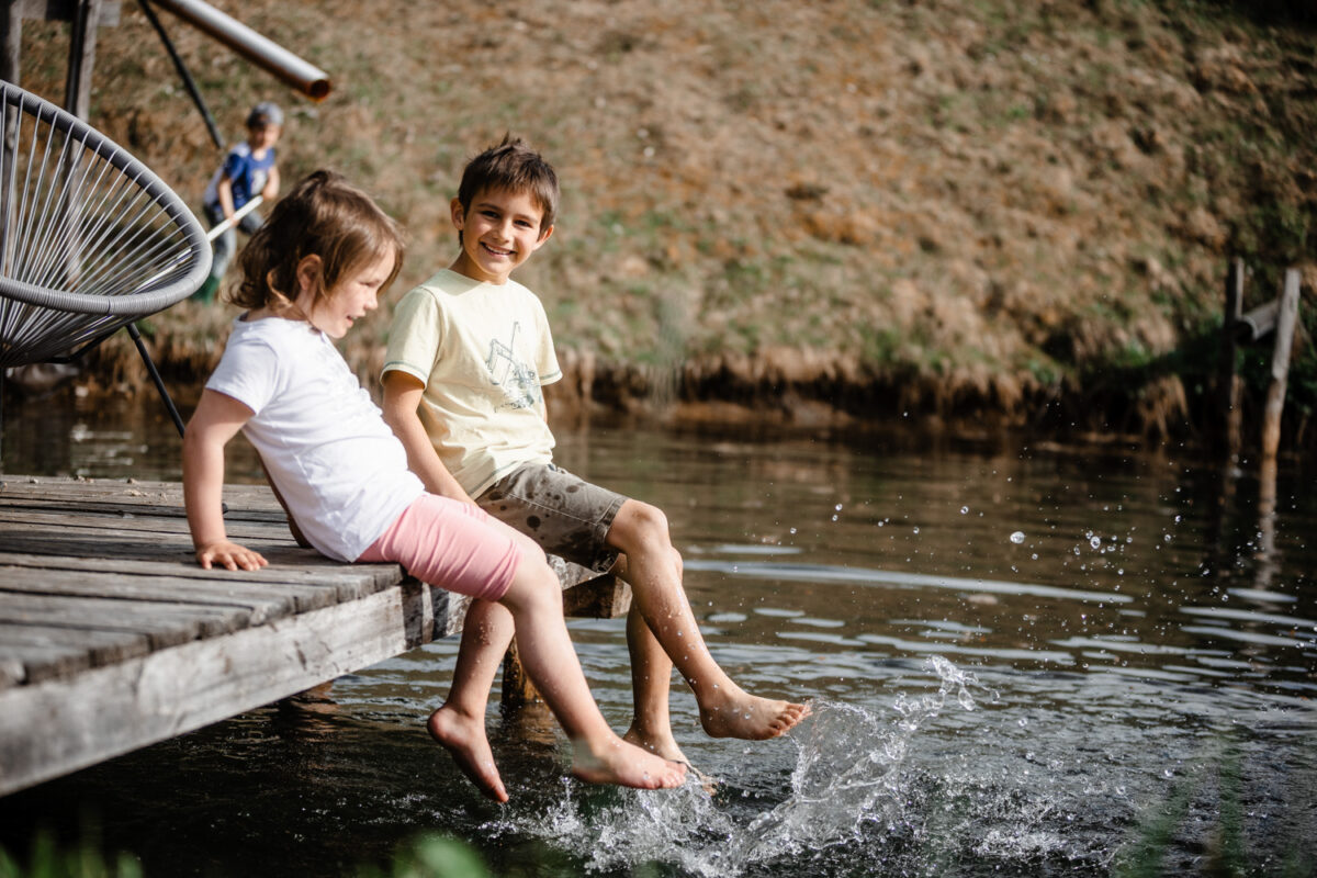 Kinder lassen am Teich die Füße ins Wasser hängen